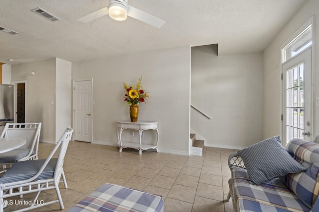 living room with ceiling fan, a textured ceiling, and light tile patterned flooring