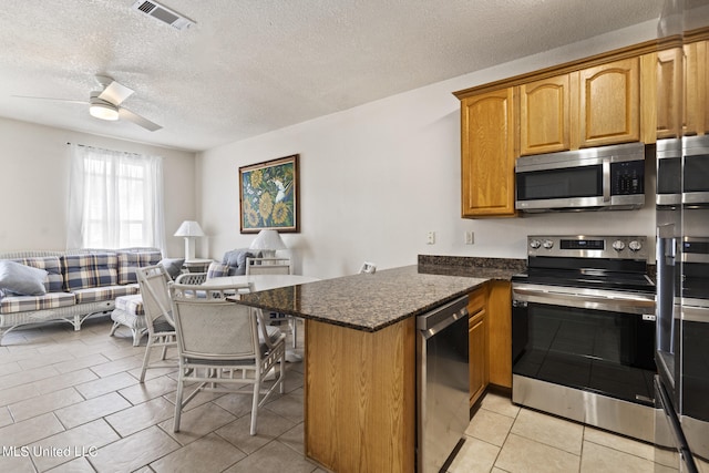 kitchen featuring kitchen peninsula, dark stone countertops, appliances with stainless steel finishes, a textured ceiling, and ceiling fan