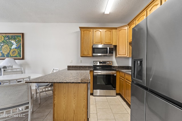 kitchen with a kitchen island, appliances with stainless steel finishes, a kitchen breakfast bar, a textured ceiling, and dark stone countertops