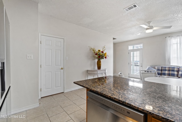 kitchen featuring light tile patterned floors, ceiling fan, a textured ceiling, stainless steel dishwasher, and dark stone countertops