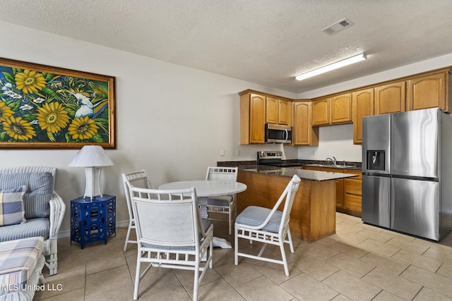 kitchen featuring appliances with stainless steel finishes, a textured ceiling, a kitchen bar, and dark stone counters