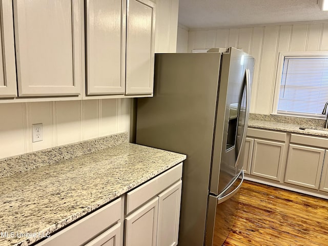 kitchen with sink, dark wood-type flooring, light stone counters, stainless steel fridge, and a textured ceiling