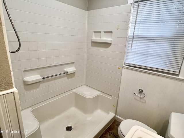 bathroom with a tile shower and toilet