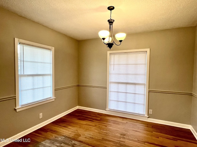 unfurnished room featuring hardwood / wood-style flooring, a textured ceiling, and an inviting chandelier