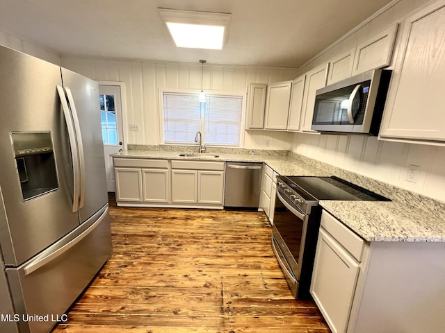 kitchen with white cabinetry, sink, hanging light fixtures, stainless steel appliances, and light hardwood / wood-style flooring