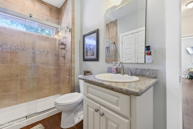 bathroom with vanity, toilet, wood finished floors, and a stall shower