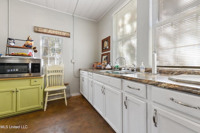 kitchen featuring dark stone counters, finished concrete floors, a sink, white cabinets, and stainless steel microwave