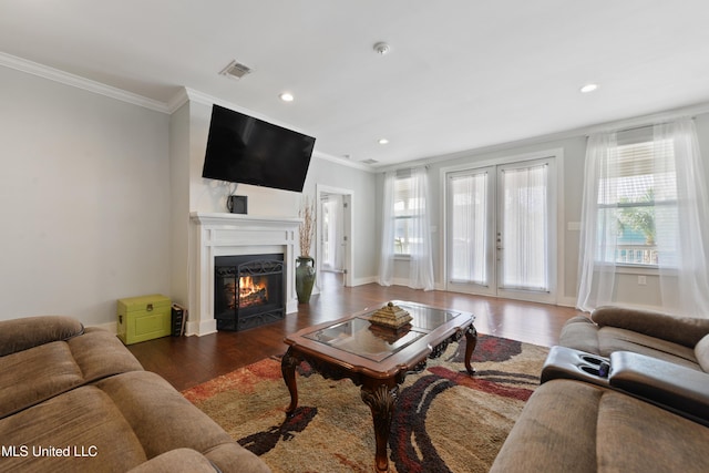 living area featuring visible vents, a warm lit fireplace, wood finished floors, and a healthy amount of sunlight