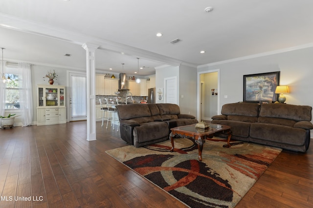 living room featuring visible vents, dark wood finished floors, crown molding, and decorative columns