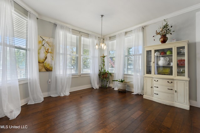 unfurnished dining area with dark wood finished floors, ornamental molding, baseboards, and a chandelier