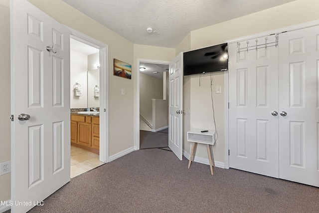 unfurnished bedroom with a textured ceiling, connected bathroom, sink, a closet, and light colored carpet