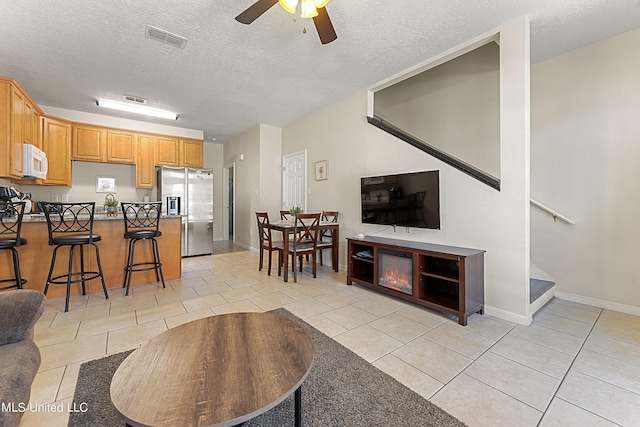 living room featuring ceiling fan, a textured ceiling, and light tile patterned flooring