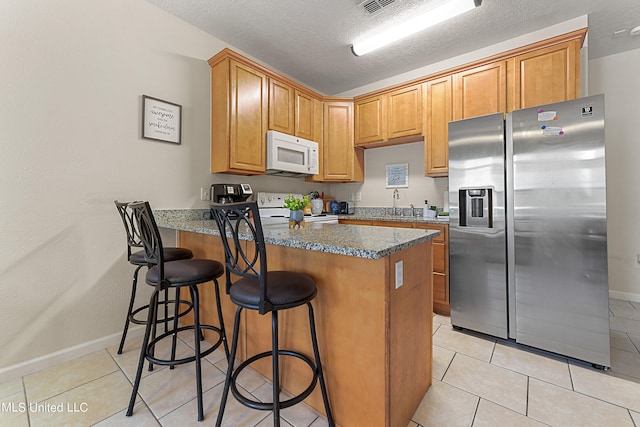 kitchen featuring white appliances, light tile patterned floors, stone countertops, a textured ceiling, and a breakfast bar area