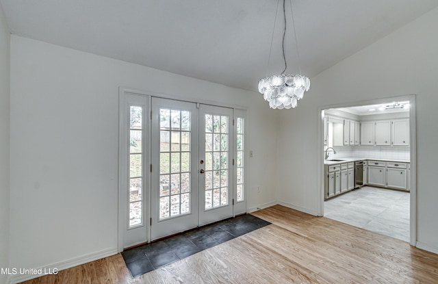 doorway to outside with an inviting chandelier, french doors, sink, vaulted ceiling, and light wood-type flooring