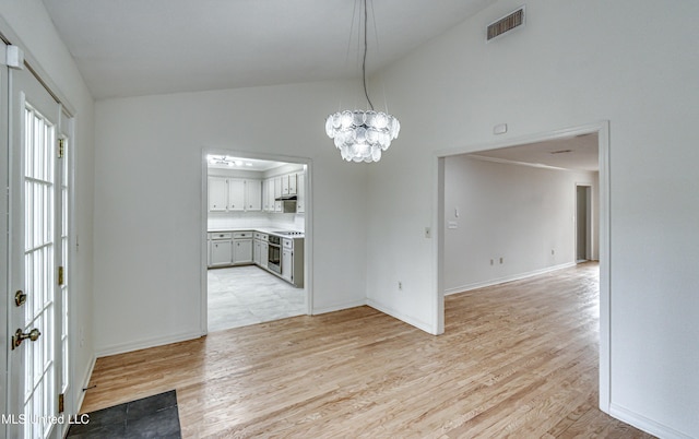 unfurnished dining area with light hardwood / wood-style flooring, high vaulted ceiling, and a chandelier