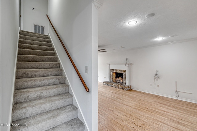 stairway featuring wood-type flooring, a textured ceiling, and a brick fireplace