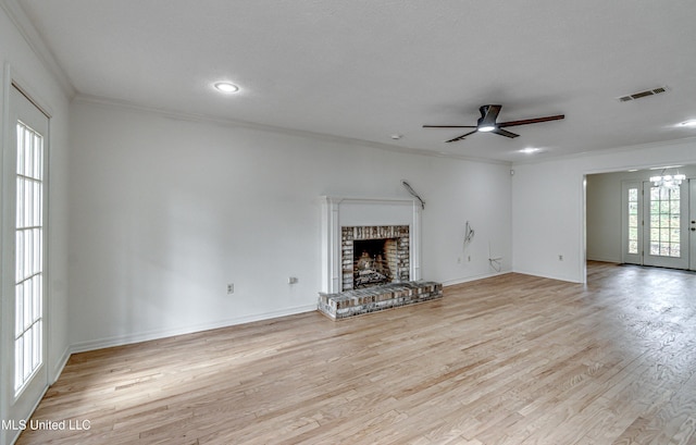 unfurnished living room featuring ceiling fan, french doors, a brick fireplace, crown molding, and light hardwood / wood-style floors