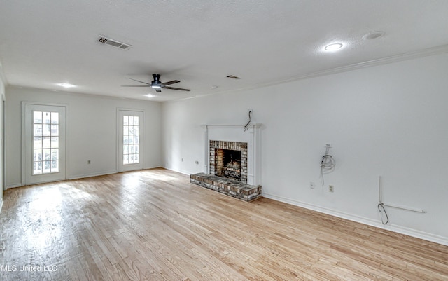 unfurnished living room featuring light wood-type flooring, a brick fireplace, a textured ceiling, ceiling fan, and crown molding