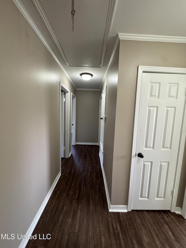 corridor with baseboards, dark wood-style floors, ornamental molding, and attic access