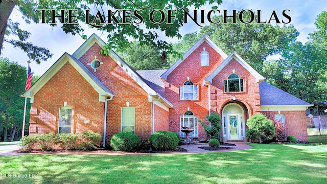 traditional-style home featuring a shingled roof, a front yard, and brick siding