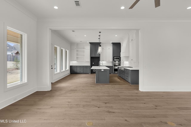 kitchen featuring visible vents, stainless steel microwave, decorative light fixtures, a kitchen island with sink, and light countertops