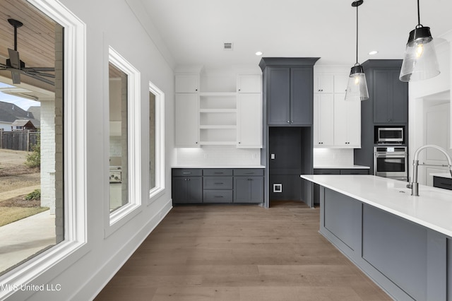 kitchen featuring appliances with stainless steel finishes, gray cabinets, light countertops, and decorative light fixtures