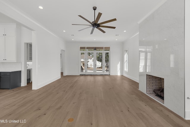 unfurnished living room with light wood finished floors, recessed lighting, a tiled fireplace, and french doors