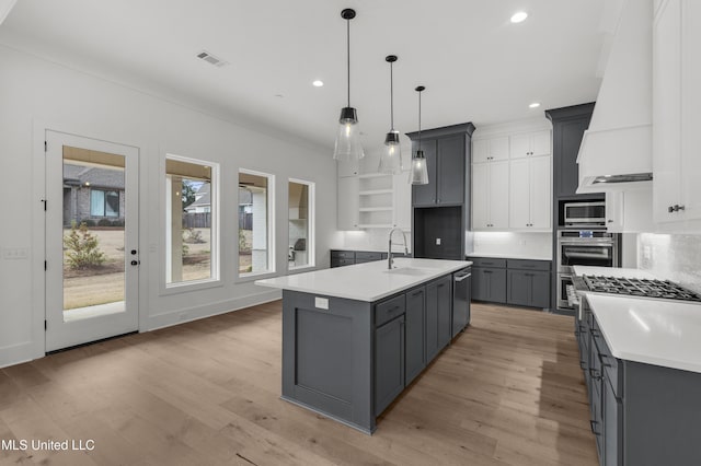 kitchen featuring visible vents, light countertops, hanging light fixtures, an island with sink, and custom range hood