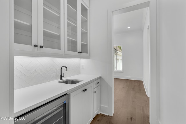 bar with beverage cooler, a sink, baseboards, decorative backsplash, and light wood finished floors