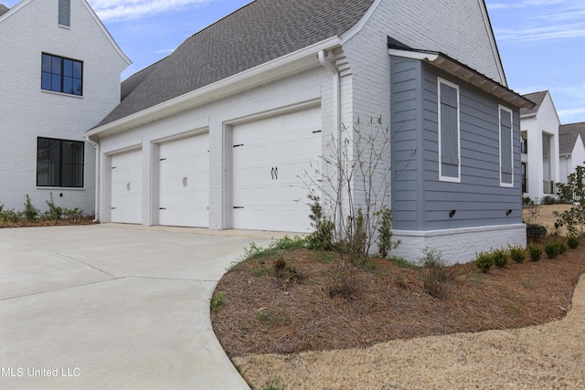 view of side of property with a garage, concrete driveway, brick siding, and a shingled roof