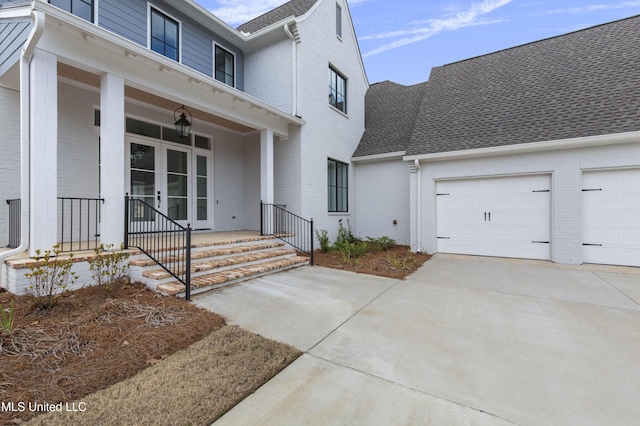 view of exterior entry featuring a porch, a garage, brick siding, a shingled roof, and concrete driveway