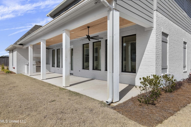 view of side of property featuring a patio area, a yard, a ceiling fan, and brick siding