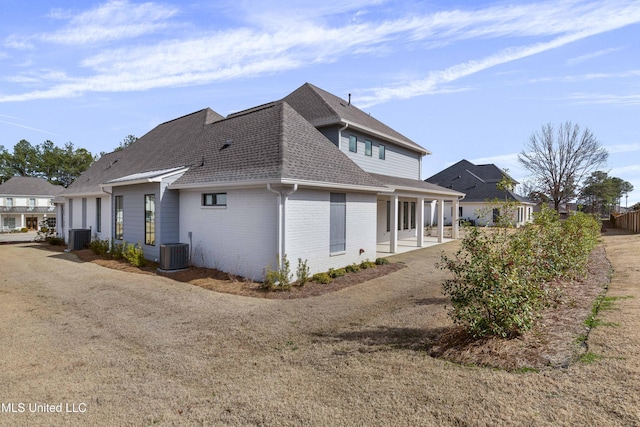 view of side of home featuring a patio area, brick siding, roof with shingles, and central AC unit