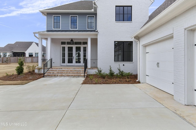 view of front of property with driveway, metal roof, a standing seam roof, french doors, and brick siding