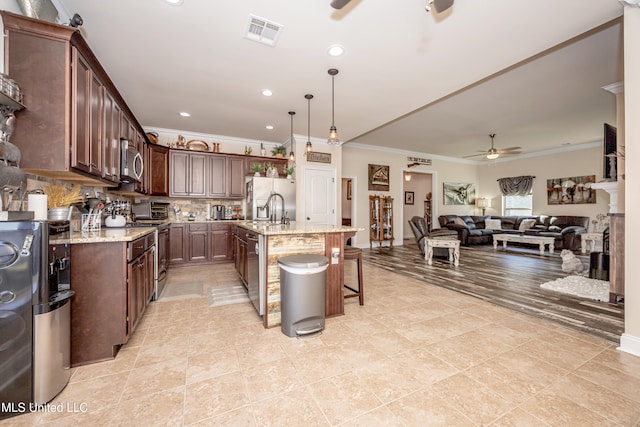 kitchen featuring ceiling fan, tasteful backsplash, an island with sink, pendant lighting, and appliances with stainless steel finishes