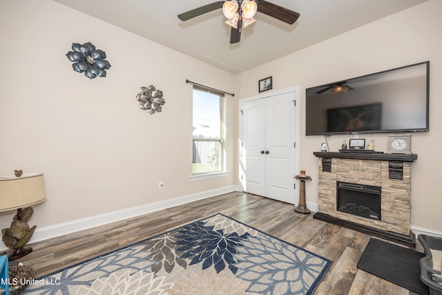 living room featuring a stone fireplace, ceiling fan, and dark wood-type flooring