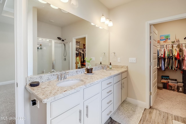 bathroom featuring double vanity, a shower stall, baseboards, and a sink