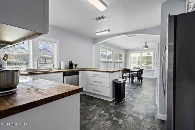 kitchen with appliances with stainless steel finishes, butcher block countertops, kitchen peninsula, white cabinetry, and ceiling fan