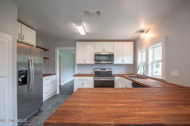 kitchen featuring sink, butcher block countertops, kitchen peninsula, stainless steel appliances, and white cabinets