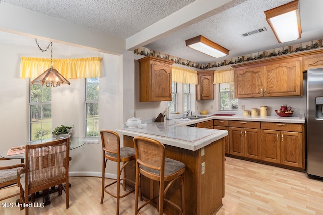 kitchen featuring kitchen peninsula, stainless steel fridge, decorative light fixtures, light wood-type flooring, and a textured ceiling