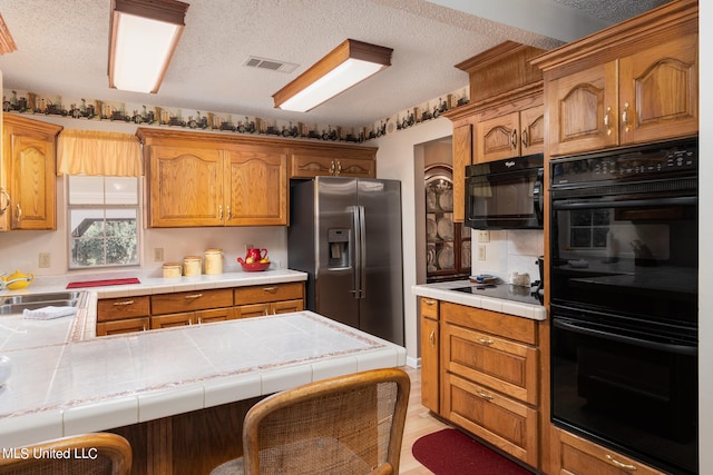 kitchen featuring tile countertops, kitchen peninsula, black appliances, and sink