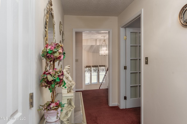 hallway with a textured ceiling, a chandelier, and dark carpet