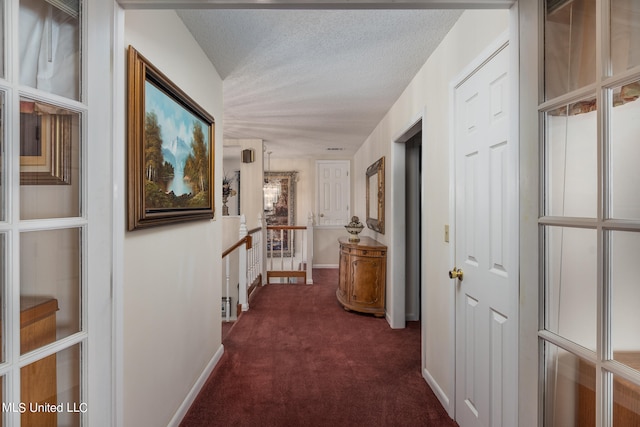 hallway featuring dark carpet and a textured ceiling