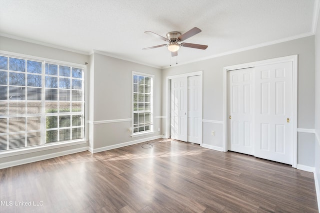 unfurnished bedroom featuring crown molding, dark hardwood / wood-style floors, and multiple closets