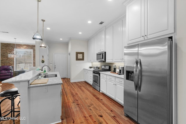 kitchen with stainless steel appliances, a center island with sink, light hardwood / wood-style flooring, white cabinetry, and hanging light fixtures