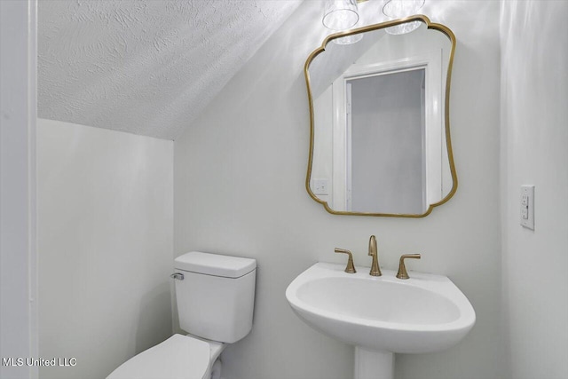 bathroom with lofted ceiling, toilet, sink, and a textured ceiling