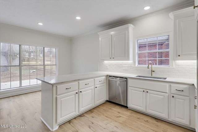 kitchen featuring sink, white cabinets, ornamental molding, stainless steel dishwasher, and kitchen peninsula