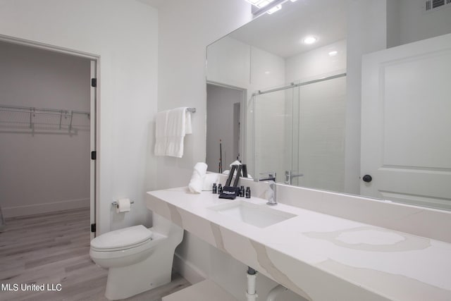 bathroom with toilet, hardwood / wood-style floors, sink, and a shower with door