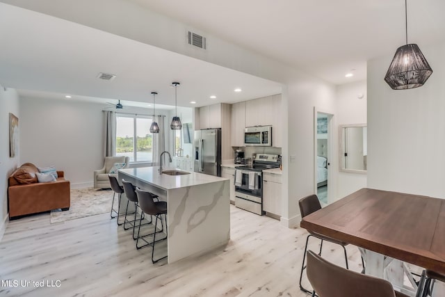 kitchen featuring appliances with stainless steel finishes, sink, light hardwood / wood-style floors, decorative light fixtures, and a center island with sink