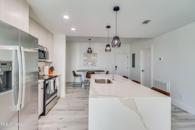 kitchen featuring light wood-type flooring, stainless steel appliances, sink, and pendant lighting